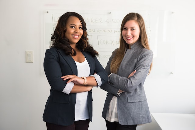 Two women in suits standing by a whiteboard