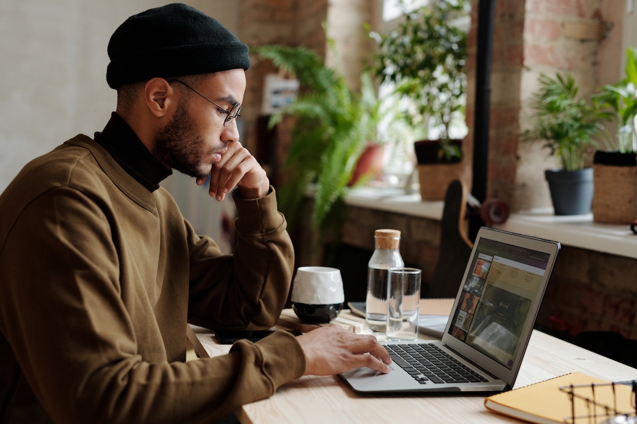 Man in brown sweater and black hat looks at laptop in preparation for working with a designer