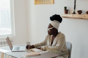 A woman using AI writing prompts at her home office desk, working on a laptop with a notebook and a cup of coffee beside her.